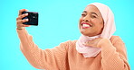 Selfie of muslim woman isolated on blue background for social media kiss, smile and emoji post online. Face of happy islamic gen z or hijab person in profile picture or influencer lifestyle in studio