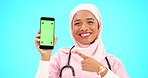 Green screen, phone and doctor isolated on blue background medical mobile app, tracking marker and mockup. Happy muslim nurse or healthcare woman face, point to cellphone product placement in studio