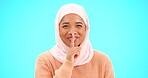 Muslim woman, finger on lips and secret with hand on mouth for mockup, advertising or promotion. Islamic female with hijab, face emoji or laugh for sale, gossip or surprise on studio blue background