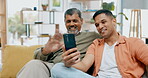 Phone, wave or video call with a man and his father sitting on a sofa in the living room of their home together. Mobile, contact or virtual chat with a senior dad and son waving to greet family