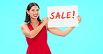 Woman holding sale poster isolated on blue background for retail, shopping or customer discount announcement. Happy face of person with fashion promotion, deal or cardboard sign in studio advertising