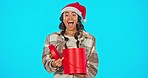 Happy, christmas and woman with a present in a studio for a festive celebration, event or party. Excited, happiness, portrait of female model with xmas gift and santa hat isolated by blue background.