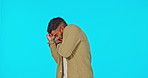 Scary, face and a man with fear of a hit isolated on a blue background in a studio. Horror, stress and portrait of a guy looking scared, expressing panic and danger of a fight on a studio backdrop