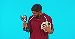 Excited, football and face of a man with a trophy isolated on blue background in studio. Happy, success and portrait of soccer player kissing an award for winning a game, achievement and celebrating