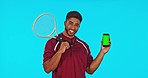 Phone, tennis and man with green screen in studio isolated on a blue background. Face portrait, racket sports and happy Indian person with cellphone for advertising, mockup and product placement.