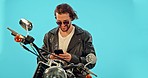 Motorbike, phone and happy man in studio on blue background for road trip, texting and leather aesthetic. Smartphone, motorcycle and man on internet for gps, location and online maps search isolated 