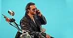 Man, phone call and motorbike in studio on blue background for road trip, freedom and fun with biker aesthetic. Smartphone, conversation and guy driver with motorcycle for vacation, journey or riding