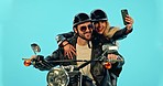 Selfie, travel and couple on motorcycle with phone for adventure, road trip and holiday on blue background. Motorbike transport, studio and man and woman take picture for social media, post or memory