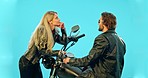 Talking, motorcycle and couple on blue background flirting, in conversation and speaking in studio. Love, dating and happy man and woman chatting on motorbike for road trip, adventure and travel