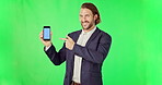 Businessman, pointing and phone on green screen with tracking markers against studio background. Portrait of happy man holding mobile smartphone display in business advertising or marketing on mockup