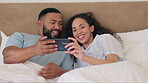 Phone, bed and happy couple streaming online, social media or mobile app for home internet or network on holiday. People or biracial woman and partner watch video on smartphone and talking in bedroom