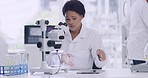 Female scientist using a microscope and tablet at a medical research lab. Focused woman looking at samples, keeping record or test results on a device. African chemist discovering a cure or treatment.