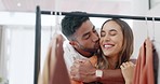 Hug, kiss and couple with wardrobe choice and clothing decision at a retail store. Happiness, smile and young woman with a man together looking at fashion, style and shop rail with a hug and love