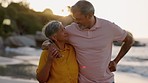 Senior couple, walking and hug on beach, summer vacation and talking for love, relax and support in sunshine. Retirement of happy man, woman and conversation at ocean, sunset and freedom with partner