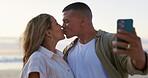 Love, selfie and couple on beach, kiss and travel for summer break, vacation and getaway. Romance, man and woman with picture for memory, happiness and bonding with romantic gesture and seaside trip