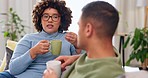 Interracial happy couple, conversation and coffee on sofa for morning bonding in living room together. Discussion, woman and man on couch with tea, quality time to relax, talk and plan day in lounge.