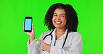 Pointing, woman and doctor with phone on green screen in studio isolated on background. Cellphone, mockup or African female medical professional with happy surprise, tracking markers or face portrait