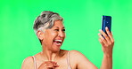 Selfie, green screen and senior woman with funny face for social media, beauty promotion and skincare. Photography, happy and elderly Indian person with natural makeup, isolated on studio background