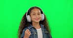 Little girl, dancing and listening to music on green screen in happiness against a studio background. Happy female person, child or kid with headphones enjoying dance, audio or sound track on mockup