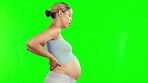 Pregnant, back pain and woman with cramps on green screen with maternity problem, worry and stress. Pregnancy, health and female person stretch in chromakey studio for contractions, backache and hurt