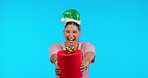 Holiday face, Christmas and a woman with a gift for happiness isolated on blue background in a studio. Happy, party and portrait of a girl giving gift for celebration or birthday with a festive box