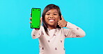 Happy little girl, thumbs up and phone mockup for social media against a blue studio background. Portrait of female child or kid smile with like emoji, yes sign or approval for mobile smartphone app