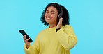 Headphones, dance and woman in a studio with music, album or playlist on her cellphone. Happy, carefree and young female model dancing e to a song, radio or track isolated by a blue background