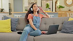 Music, woman with laptop and headphones listen on sofa in living room of her home. Technology or connectivity, streaming media and happy female person listening to radio or podcast on a couch