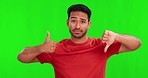 Green screen, thumbs up and down and confused Asian man with doubt, decision and choice in studio. Unsure, hand sign and portrait of male person on chromakey background with vote, review and feedback
