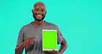 Black man, tablet and pointing on green screen for advertising on mockup against a studio background. Portrait of happy African male person show technology chromakey display and tracking markers