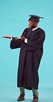 Marketing, graduation and male student in a studio showing a promotion or advertisement. Happy, smile and young African man graduate with a presentation hand gesture isolated by a blue background.