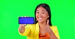 Green screen, phone screen and woman face with thumbs up for yes, vote or social media review on studio background. Portrait, smile and asian lady with emoji hand or smartphone networking promo offer