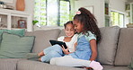 Tablet, kids and sisters playing games online while sitting on a sofa in the living room of their home together. Children, technology and girl siblings streaming an online video while bonding for fun