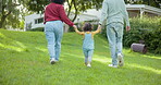 Family, walking and parents support a child in a backyard bonding by a home or house for care or love for a holiday. Outdoor, mother and father enjoying quality time and playing with kid in back view