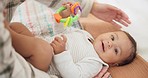 Baby child, rattle toys and bed with mother, playing or care in family home for learning with childhood development. Portrait, infant kid and excited for games, bonding and happy with mom in nursery