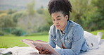 Black woman, reading and relax with a book in the park, nature on a study break, rest and research on university campus. Girl, learning a story and college textbook, novel or literature for class