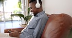 Headphones, sofa and man listening to music, playlist or radio while networking on a phone. Happy, cellphone and African male person streaming song or album while browsing on social media or internet