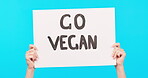 Hands, poster and vegan propaganda on a blue background in studio for health, diet or nutrition awareness. Sign, news and politics with a person holding a billboard in protest of animal cruelty