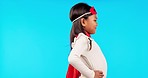 Superhero, fantasy and girl child in a studio with a cape and face mask with wind blowing. Save, happy and profile of a kid model in cosplay outfit or costume isolated by blue background with mockup.
