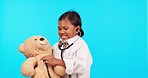 Child, doctor and teddy bear in a studio with medical check, stethoscope and patient analysis. Young girl, help and smile with blue background and healthcare, hospital and clinic coat for pretend fun
