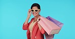 Sunglasses, shopping bag or happy woman with gift in studio on blue background with cool clothes. Face portrait, smile or rich girl with present or product on discount deal or promotional sales offer
