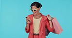 Phone, shopping bag or happy woman on social media for online fashion in studio on blue background. News, smile or rich girl with sunglasses or notification on discount deal or promotional sale offer