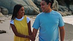 Happy couple, holding hands and walking on beach for holiday, weekend or break together in nature. Man and woman smile on a ocean walk by the coast enjoying bonding, quality time or relax in outdoors