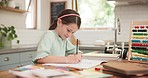 Child, homework and student education writing in notebook with knowledge development. Paper, study and learning at a table with math problem and books for school and drawing in a kitchen in home