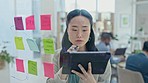 Business, asian woman and thinking at glass with tablet, notes of solution or research objectives in office. Female employee writing ideas, planning timeline or brainstorming with digital technology