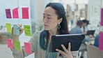 Asian woman, tablet and writing on glass board for schedule planning or sticky note tasks at office. Female person with technology in brainstorming, strategy or mind map for project plan at workplace