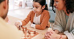 Child, mother and family playing chess at home while teaching or learning board game. Latino woman and girl kid at table together to play for fun, checkmate or competition for quality time or bonding