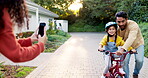 Mother, father and kid on bike learning in driveway with phone to record video, photograph or family support. Excited parents teaching happy girl on bicycle with mobile for memory, fun games and care