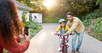 Happy family, parents and teaching kid on bicycle with phone to record video, photograph and childhood growth. Mom, dad and memory of girl learning to ride bike with support, play and development