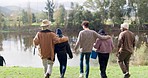 Friends, back and walking by camping lake in nature for bonding, fishing and summer picnic by woods. Happy men, women or group of people in diversity by water in forest for travel, holiday or freedom